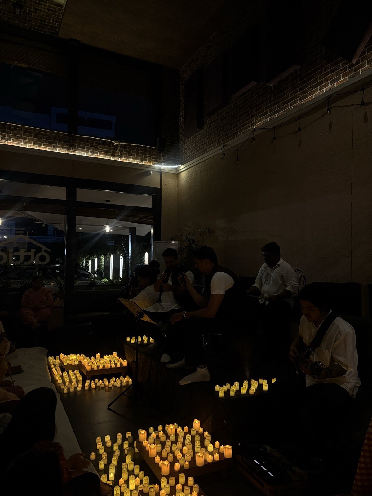 Musicians playing guitar and singing from lyric sheets around candlelight.