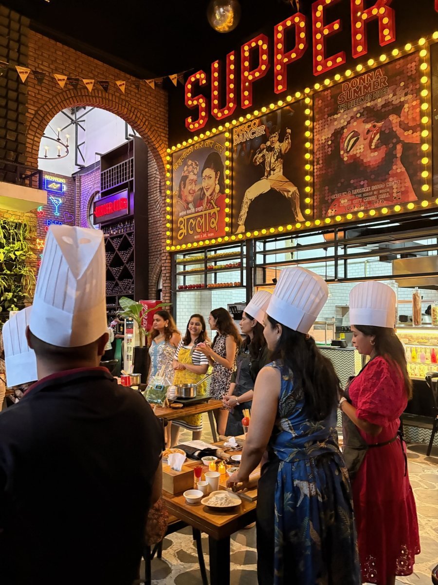 Guests in chef hats at the prep table under the venue sign.