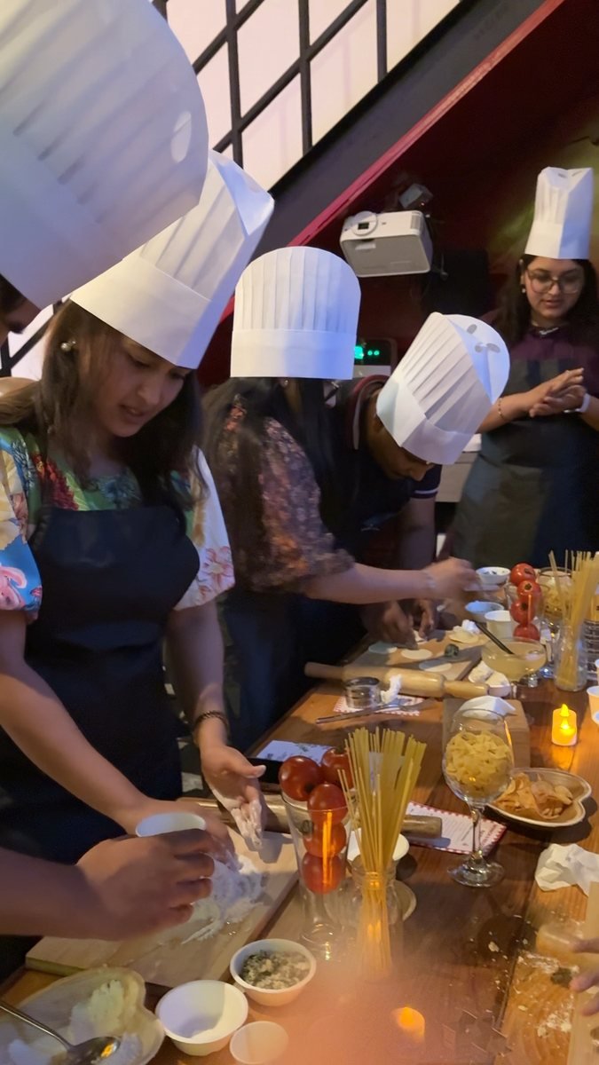Hands working dough beside spaghetti, tomatoes and herbs.