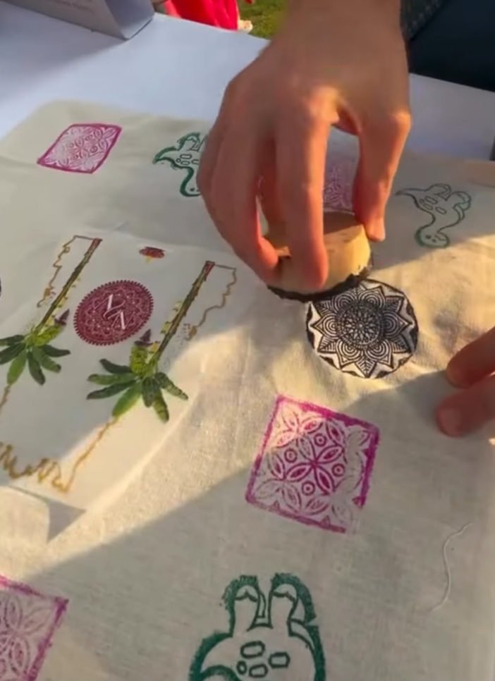 A hand pressing a carved wooden block onto cotton fabric.