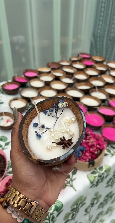 A coconut-shell candle set with dried flowers, held to camera.
