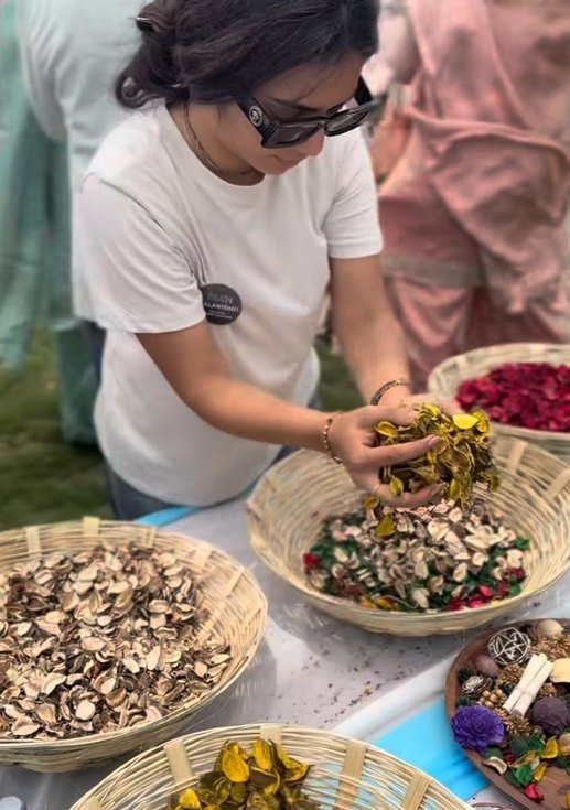 A guest mixing dried petals and botanicals from open baskets.